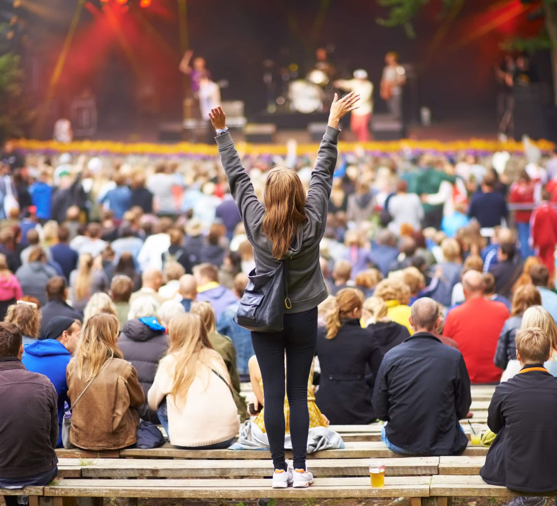 Rear-view shot of a crowd at an outdoor music festival with the focus on a female fan cheering